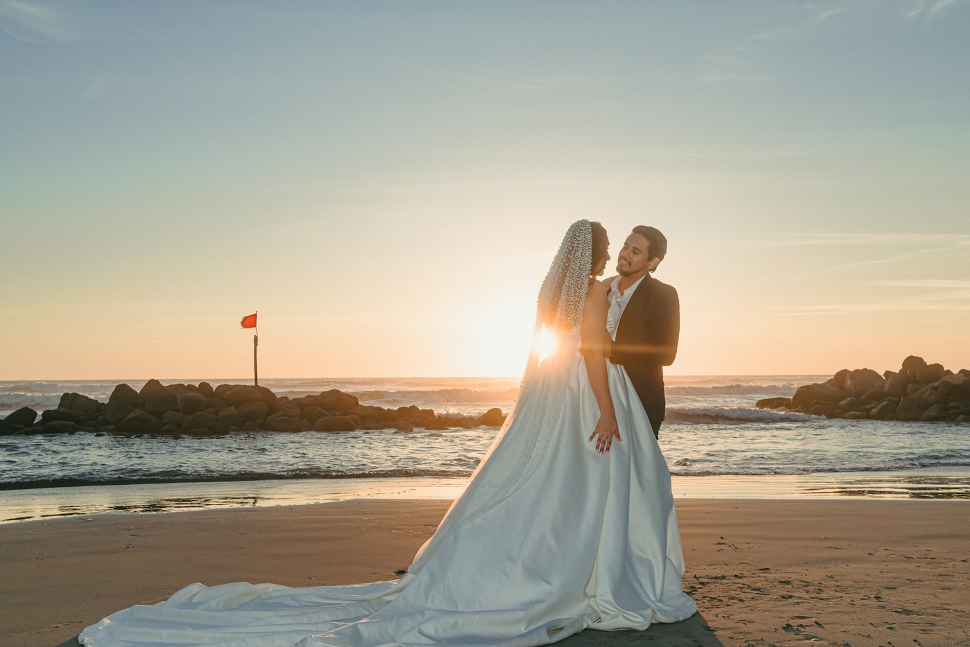 A wedding couple embracing on the beach at sunset